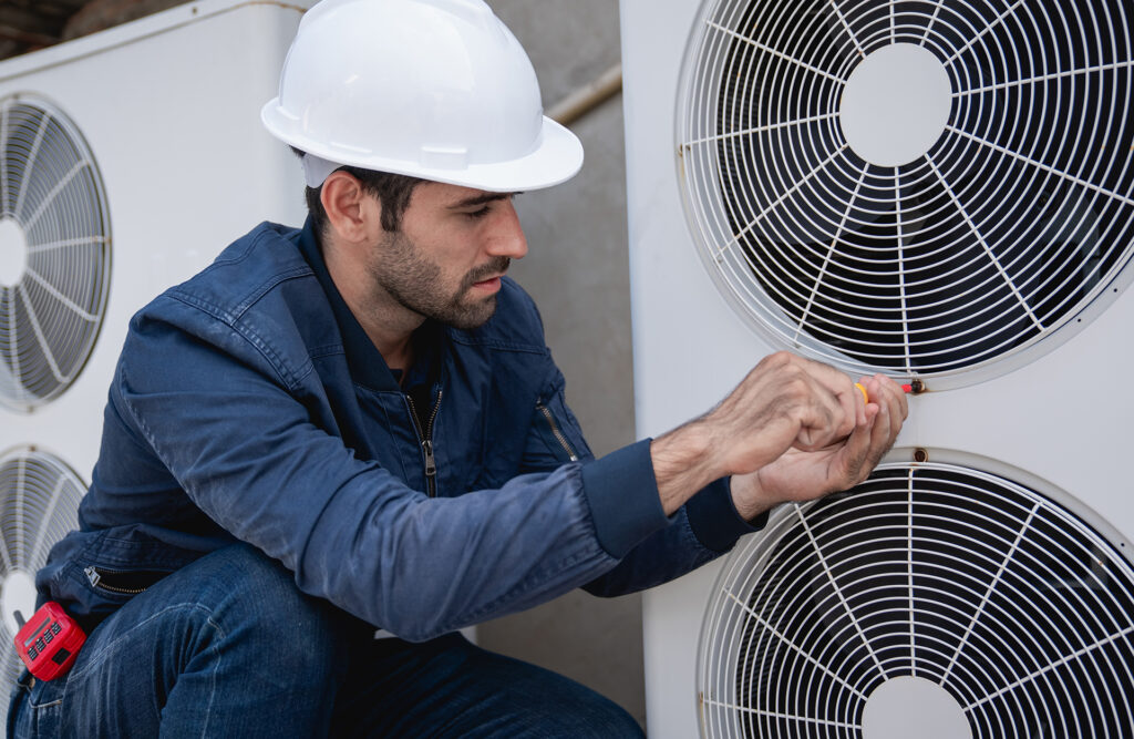 Online Clima, venta de equipos de aerotermia en Puertollano. Electricista con casco blanco desatornillando un tornillo de un motor de aire acondicionado doble.