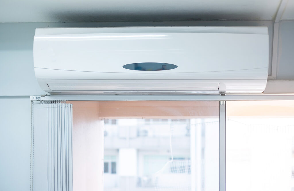 Online Clima, venta de equipos de aerotermia en Puertollano. Equipo de aire acondicionado moderno blanco junto a una ventana blanca.